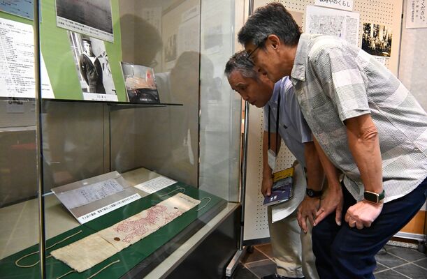 展示された亡き義父の千人針を前に、大塚さん(左)から説明を受ける吉成さん=10日午前、宇都宮市本丸町