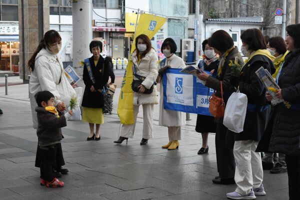 親子連れに啓発チラシやミモザの花を配る参加者＝８日午後、宇都宮市江野町
