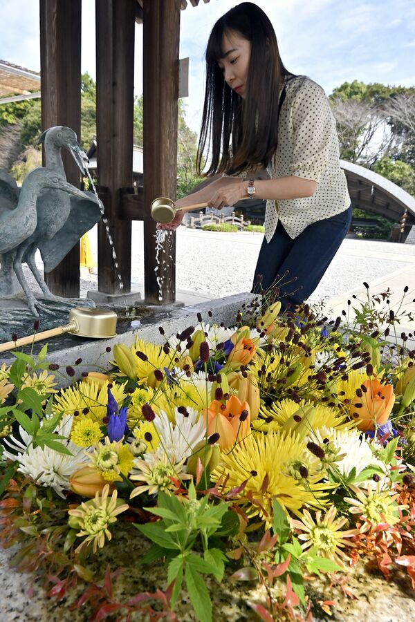 色鮮やかな花が生けられた手水舎で手を清める参拝客＝29日午前11時10分、上三川町しらさぎ１丁目