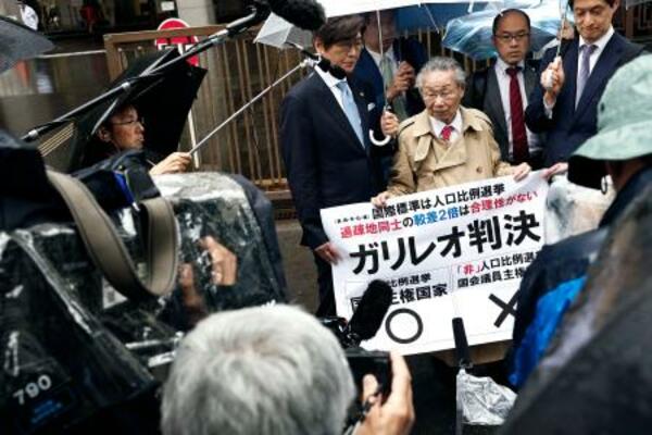 衆院選「1票の格差」訴訟の判決を受け、東京高裁前で「ガリレオ判決」などと書かれた紙を掲げる升永英俊弁護士(前列右から2人目)ら=21日午後