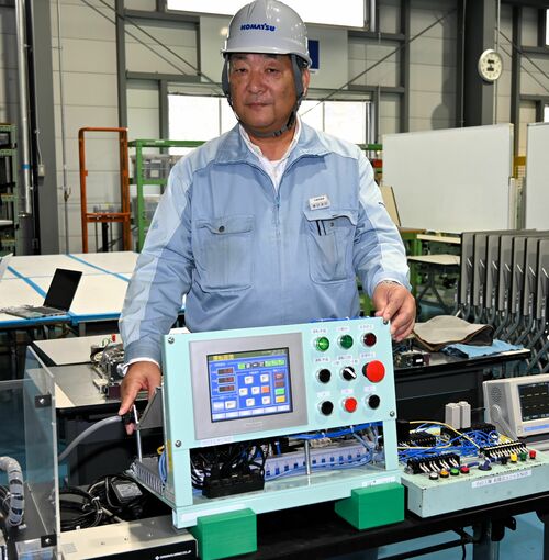 電気回路の検定機器に手を添える諏訪さん＝コマツ小山工場