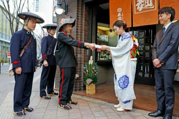 　明治時代の制服に身を包んだ配達員から年賀状を受け取るうどん店「三国一」の橋本有希野さん＝１日午前、東京都新宿区
