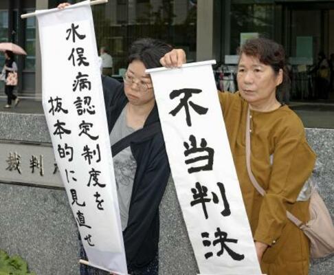 　水俣病患者認定を巡る訴訟の判決で、「不当判決」などと書かれた紙を掲げる支援者ら＝２３日午後、福岡高裁前
