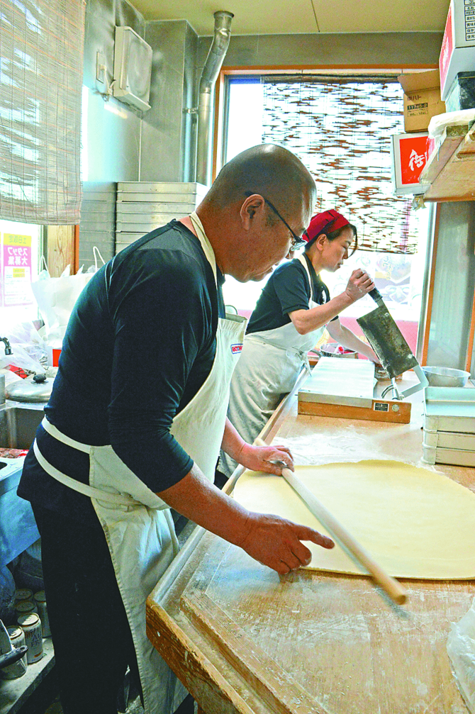 うどんの生地を延ばす斉藤芳則社長（写真手前）