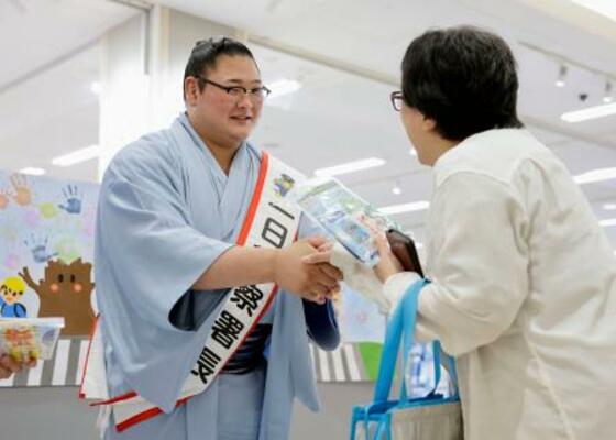 地元住民(右)に交通安全グッズを手渡し握手する欧勝海関=26日午前、石川県津幡町