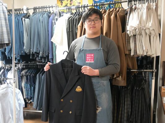 宇都宮市学生服リユースｓｈｏｐリボンに並ぶ制服と、運営を手伝う皆川理事長の次男奏さん＝７日午後、宇都宮市内