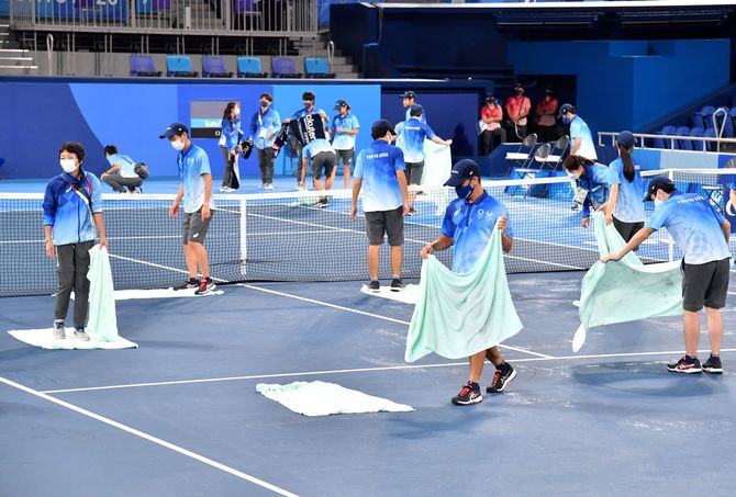 雨にぬれたコートを拭うスタッフたち。スムーズな試合運営のため、奔走した＝９月１日午後２時５分、有明テニスの森公園