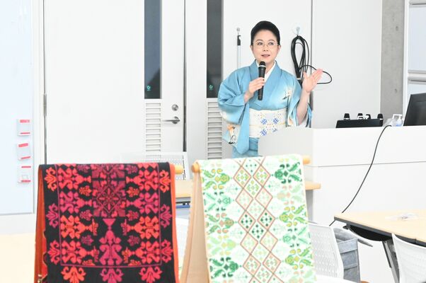 講演する山本代表とパレスチナの伝統刺繍の着物帯＝20日午後４時35分、宇都宮市陽東７丁目