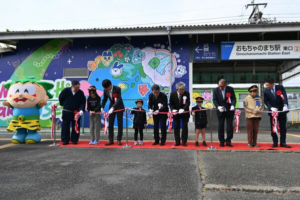 ラッピングされたおもちゃのまち駅の前でテープカットをする関係者ら=27日午前、壬生町幸町1丁目