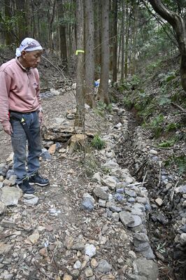 泥出しし、石積みを施した里山再生のための水路について説明する田中さん