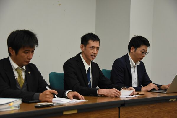 記者会見で労働審判や仮処分の申し立てについて語る當間さん（中央）＝18日午後、県庁記者クラブ