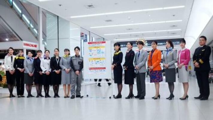 　モバイルバッテリーの取り扱い変更を周知するポスターと航空各社の社員ら＝１４日午後、羽田空港