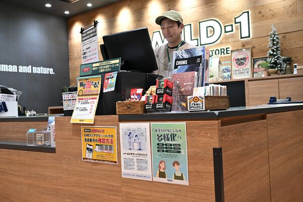 商品の帽子をかぶって勤務する高橋さん。カウンターには、身だしなみの多様化を知らせるポスターが掲示されている＝12月下旬、ワイルドワン宇都宮西川田店