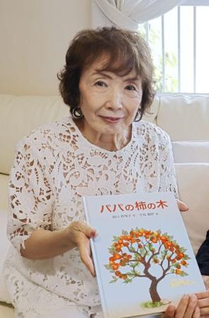 絵本「パパの柿の木」の改訂版を手にする谷口真知子さん＝６月、大阪府箕面市