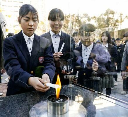 「1・17希望の灯り」の分灯が始まり、ろうそくに火を移す中学生=10日午後、神戸市中央区の東遊園地