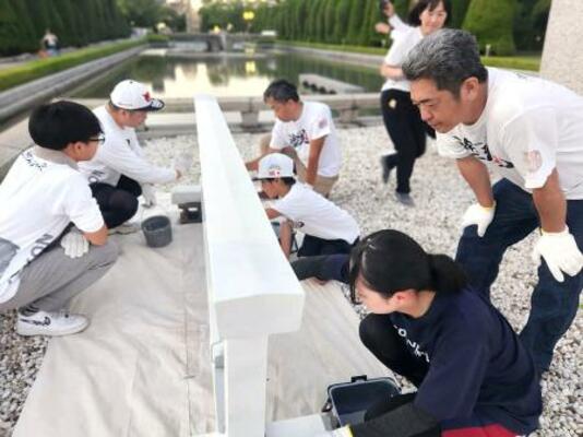 広島市の平和記念公園で柵を白く塗るボランティア=2025年7月(塗魂ペインターズ事務局提供)