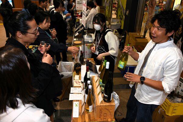 ワイナリー関係者（右）の説明を聞きながら栃木ワインを試飲する来場者＝18日午後、JR宇都宮駅ビル