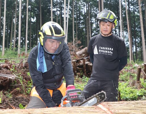 白石専務（右）の指導を受けながら造材作業に挑む記者