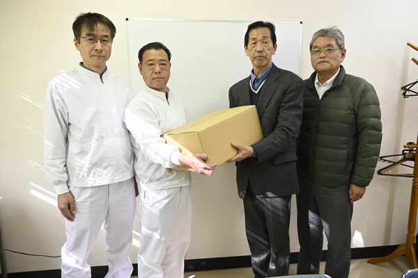野沢工場長（左から２人目）から寄付品のカレーを受け取る君嶋会長（同３人目）