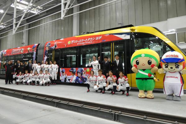 １日から運行開始するラッピング列車の前で記念撮影する選手ら