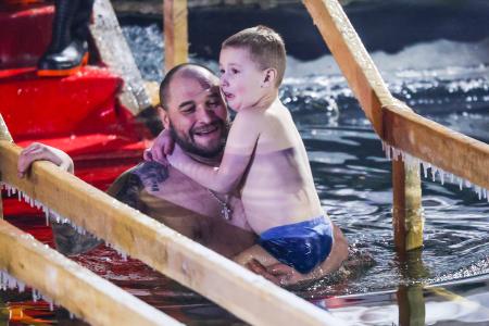 　ロシア正教の「主の洗礼祭」に合わせ、子どもを抱いて沐浴する男性＝１８日、モスクワ（タス＝共同）