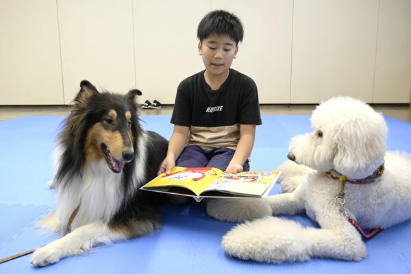 セラピー犬に寄り添ってもらいながら絵本を読む子ども