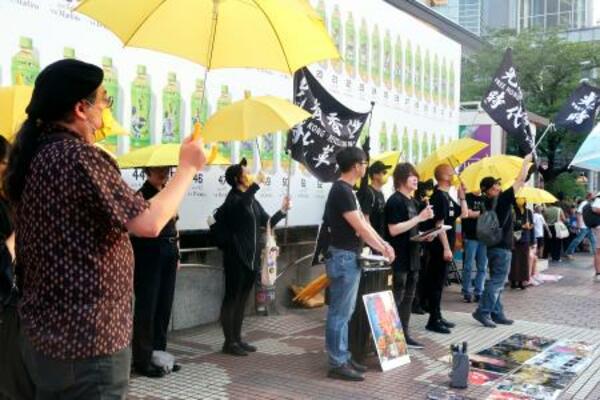 東京・渋谷駅前で開かれた在日香港人らの集会で、黄色い傘を掲げる参加者=13日午後