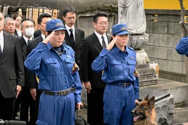 　慰霊碑の前で敬礼する警察犬の担当者＝２３日午前、東京都板橋区