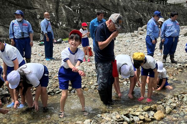 簡易いけすで魚をつかみ川に放流する児童ら