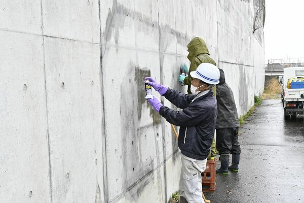 手作業でコンクリート壁の落書きの除去していく作業員