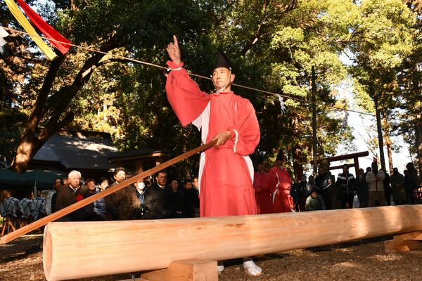 ご神木の前に立ち、宙に指で文字を書く大工