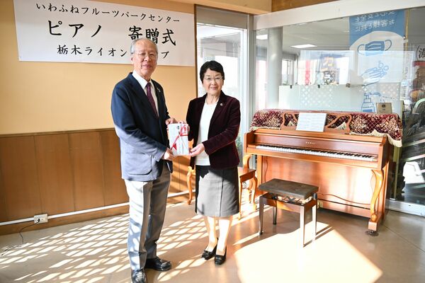 大川市長に目録を手渡す長谷川会長（左）と寄贈されたピアノ