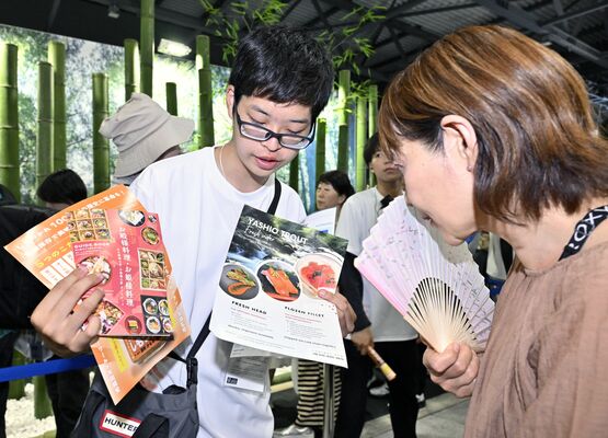 来場者に飲食メニューを説明する小堀絢心さん（左）＝28日午後３時25分、大阪市此花区の夢洲