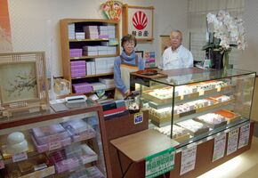 さまざまな菓子が並ぶ店内に立つ阿久津慎さん（右）と知子さん