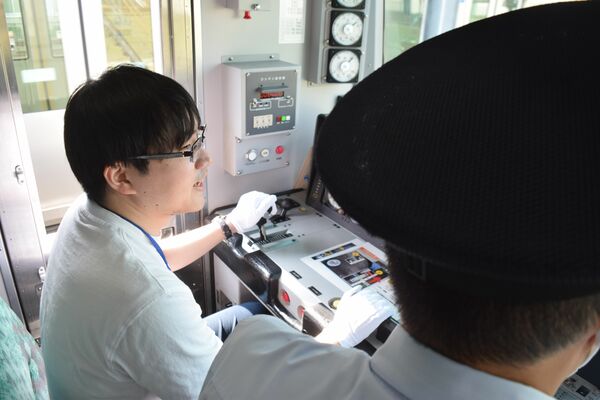 運転士の指示を受けながらアキュムを運転する参加者（左）＝27日午後、宇都宮市