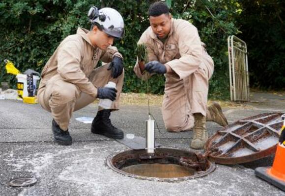 白い泡が出ているのが見つかったマンホールを調査する米軍関係者=29日午後、沖縄県宜野湾市