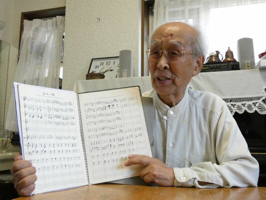 当時の楽譜を見せ、石山の歌を口ずさむ鈴木さん