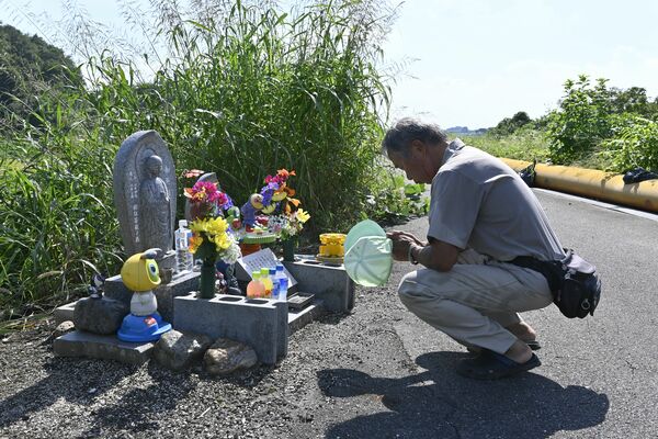 地蔵に手を合わせ兄弟の死を悼む市民。事件発生20年のこの日、訪れた人が線香や飲み物を供えた＝12日午後１時55分、小山市間中