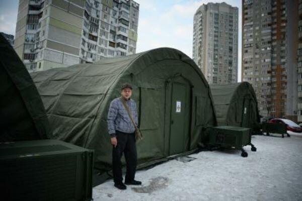 25日、ウクライナ・キーウに設けられた緊急暖房設備の前に立つ地元住民(ゲッティ=共同)