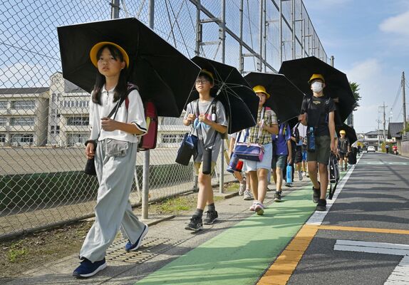 傘を差し、暑さをしのぎながら下校する児童たち=14日午後3時40分、壬生町落合3丁目