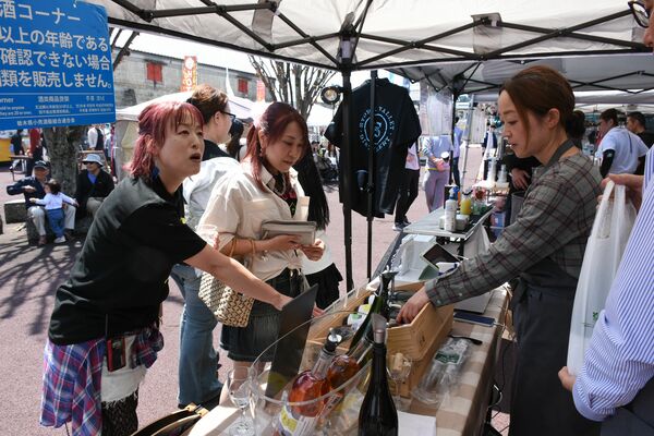 各出店ブースを巡り、声を掛ける星絵理子さん（左）＝４月２６日、ＪＲ宝積寺駅前