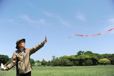 紙飛行機とカタパルトを手に、風を読む永井義章さん=東京都葛飾区