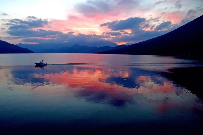 日没時、静寂の中禅寺湖を船が横切る。波紋で湖面に映る空が揺れた