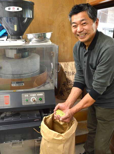 石臼でひく収穫したての玄ソバを手に取る安田会長