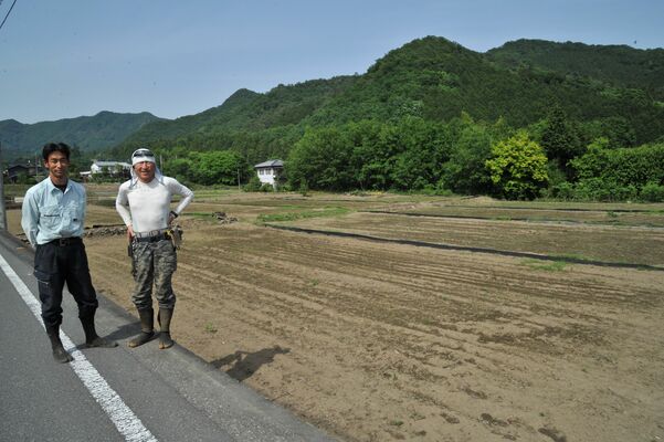 田植えが行われる田んぼ（後方）と閑援隊の川元隊長（左）ら