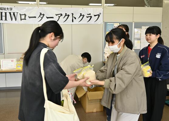 国福大生(左)に新米を手渡す同大RACのメンバー