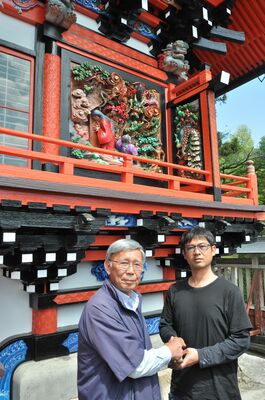 塗り直された社殿の彫刻画の前で、握手を交わす福島さん（左）と片山さん