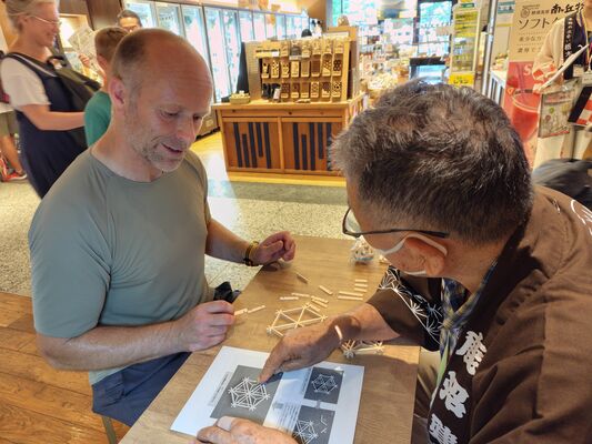 豊田さん（右）から鹿沼組子のコースター作りを指導してもらう来場者＝27日午後、東京都墨田区