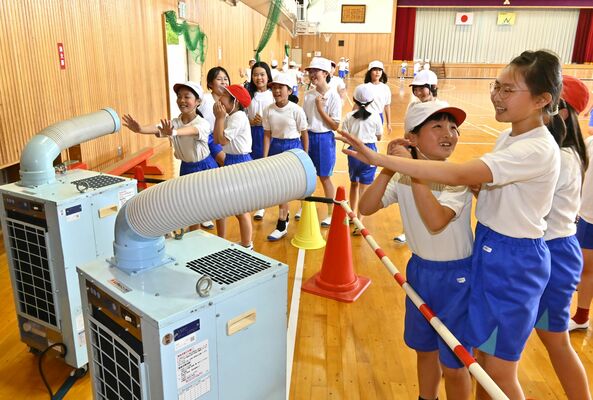 授業の合間にスポットクーラーで涼む児童ら
