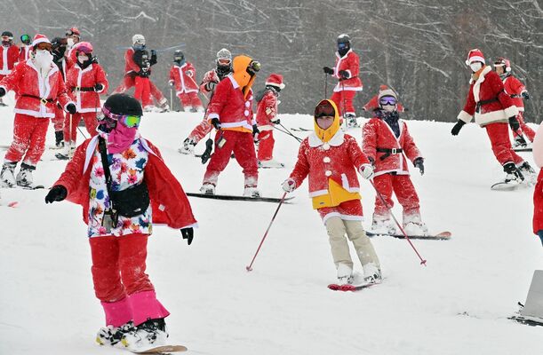 雪が降る中、サンタ姿で滑走する来場者たち＝24日午前10時50分、那須町大島